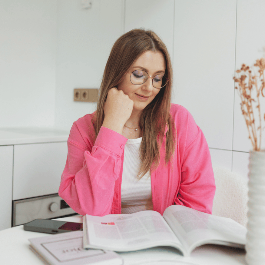 Patrycja siedzi przy stole z książką. Zdjęcie profilowe Patrycja Marszalec.